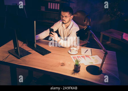 Parte superiore al di sopra di un angolo alto visualizza foto di un uomo con gli occhiali occhiali a lavorare fino a tarda notte prima di personal computer analizzando i dati salvati sul telefono con dati su Foto Stock