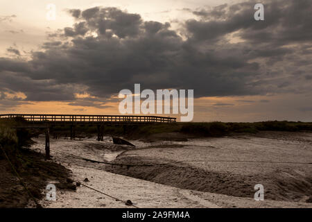 Un suggestivo moody salt marsh a bassa marea con un ponte pedonale che attraversa un fangoso dyke Foto Stock