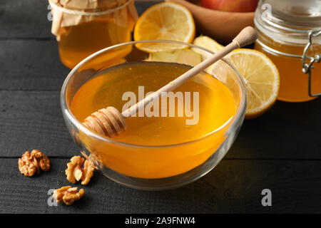 Ciotola con il miele, bilanciere e noce su sfondo di legno, close up Foto Stock