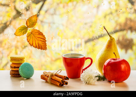 Amaretti, tazza di caffè, bastoncini di cannella, pera, mela e foglia secca sul vetro del finestrino con gocce d'acqua in sfondo sfocato. Foto Stock