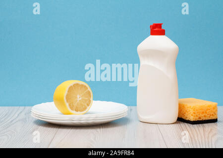 Bottiglia di plastica di detersivo liquido per stoviglie, pulire le piastre, limone e spugna su sfondo blu. Il lavaggio e la pulizia di concetto. Foto Stock