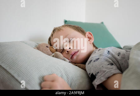 Giovane ragazzo dormire con il suo recare nel letto di casa Foto Stock