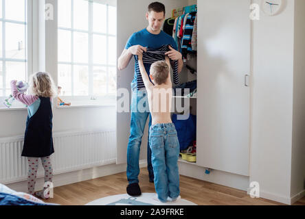 Padre aiutando i suoi bambini si vestono la mattina pronti per la scuola Foto Stock