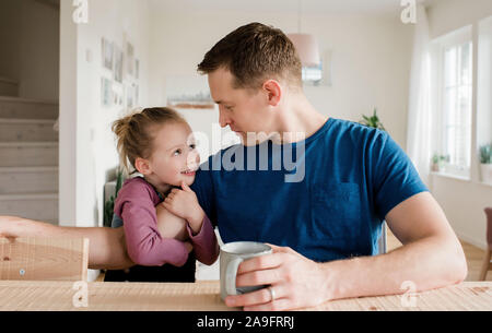 Bambina cuddling suo papà la mattina prima della scuola Foto Stock