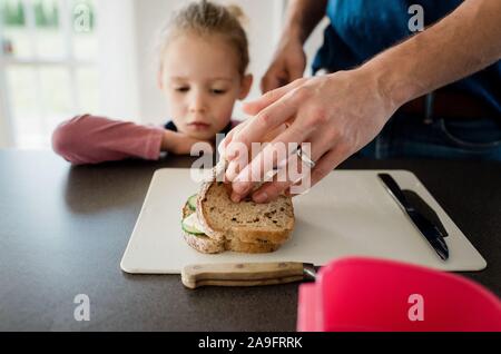 Padre rendendo i suoi bambini pranzo al sacco per la scuola mentre guarda figlia Foto Stock