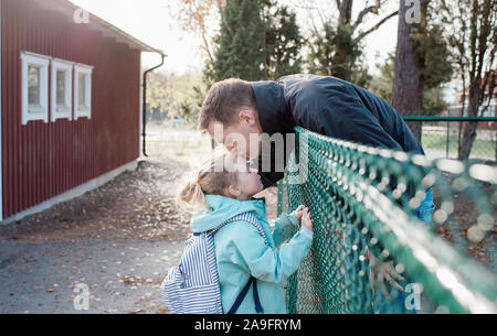 Padre baciare la figlia addio al cancello della scuola Foto Stock