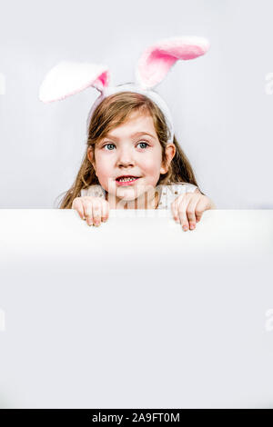 Felice carina ragazza del bambino in un costume di coniglio con Orecchie di lepre con un paniere di uova dipinte di picchi fuori da dietro la parete. Il giorno di Pasqua concetto. Sfondo Foto Stock