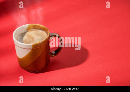 Brown tazza da caffè con vapore su sfondo rosso. Composizione sparse Foto Stock