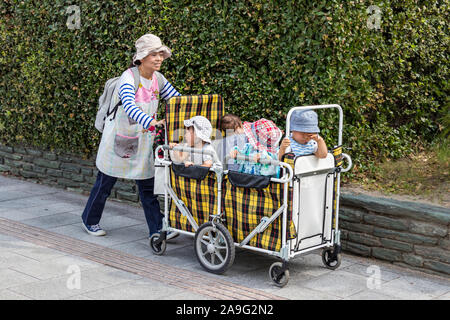 Un giapponese di babysitter - insegnante di scuola materna che porta quattro bambini su un carrello per una passeggiata. Foto Stock