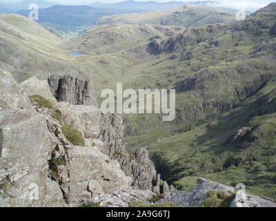 Vista del paesaggio attraverso il parco nazionale del Lake District da una rocciosa battuta scoscese verso verdi colline con una valle e il lago sottostante Foto Stock