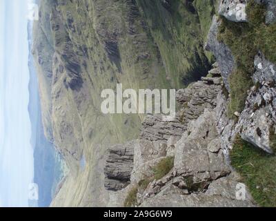 Vista del paesaggio attraverso il parco nazionale del Lake District da una rocciosa battuta scoscese verso verdi colline con una valle e il lago sottostante Foto Stock