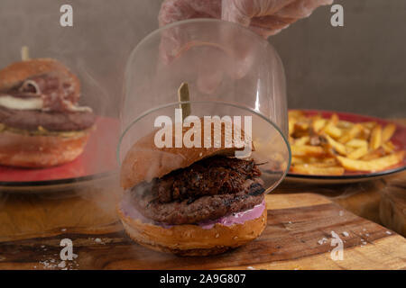 Close-up di mano dello chef il sollevamento di un contenitore in vetro di deliziosi piatti fatti in casa fame affumicato con trucioli di legno da Jack Daniel's, shredded barbecue di carne di maiale e di American sa Foto Stock