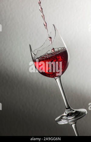 Studio closeup di riempimento di vino rosso in una rottura di un bicchiere di vino davanti a trama sfondo con morbida luce-buio gradiente. Foto Stock