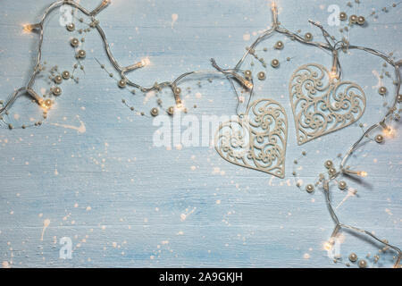 Natale o composizione d'inverno. Modello realizzato di ornamenti in forma di cuore e di luci decorato con perle su luce strutturata sfondo blu. Christma Foto Stock