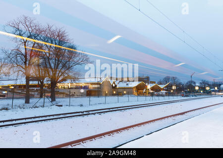 TALLINN, Estonia - 23 dicembre 2018: Le rotaie e le strisce di luce di passaggio di treni su nevoso inverno sera a Tallinn in Estonia su dicembre 23, 2018 Foto Stock