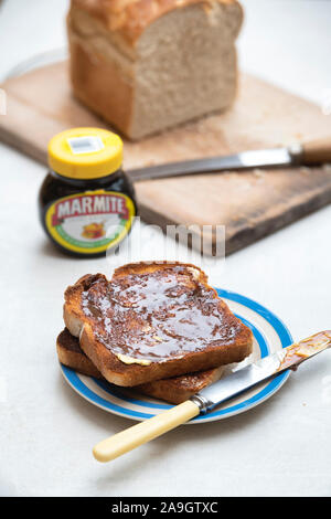 Marmite su toast sulla piastra vicino ad una pagnotta di pane bianco e un vaso di marmite Foto Stock