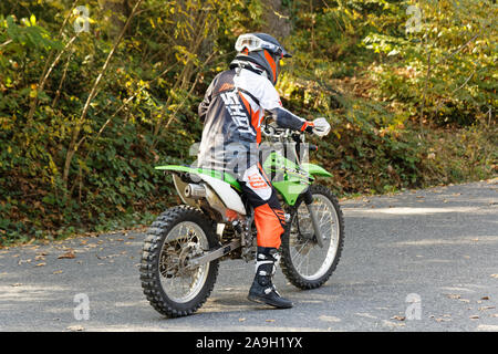 Il pilota di motocross con abbigliamento protettivo in attesa su strada nella foresta Belgrad in autunno. Vista dal retro. Foto Stock