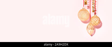 Banner con tre golden baubles di Natale appeso contro lo sfondo rosa. In stile minimale Anno nuovo concetto. Foto Stock