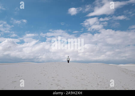 Uomo in un abbigliamento informale tra le dune di sabbia bianca contro il cielo blu Foto Stock