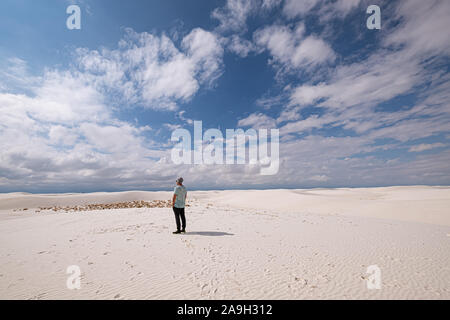 Uomo in un abbigliamento informale tra le dune di sabbia bianca contro il cielo blu Foto Stock