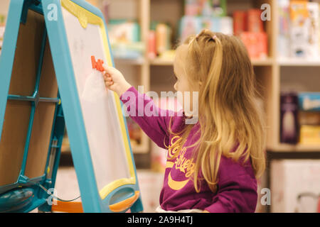 Adorabile bambina disegna sulla scrivania in negozio per bambini. Foto Stock