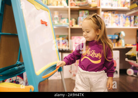 Adorabile bambina disegna sulla scrivania in negozio per bambini. Foto Stock