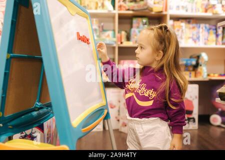 Adorabile bambina disegna sulla scrivania in negozio per bambini. Foto Stock