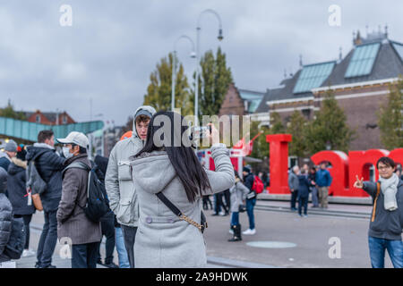 Amsterdam, Olanda, ottobre 2018, ragazza scatta una foto del ragazzo sul mio segno di Amsterdam di Amsterdam, di fronte al Rijksmuseum con lei cellphon Foto Stock