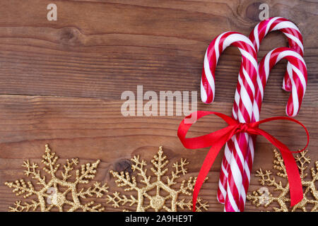 Natale greeting card modello con un mazzetto di caramello rosso canne e golden i fiocchi di neve su un sfondo di legno Foto Stock