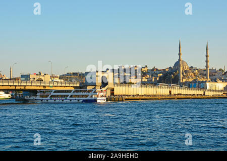 Istanbul,Turkey-September 6 2019. Il traghetto passa sotto il Ponte di Galata basso nel tardo pomeriggio di sole estivo. La Moschea Yeni o una nuova moschea è sulla destra Foto Stock