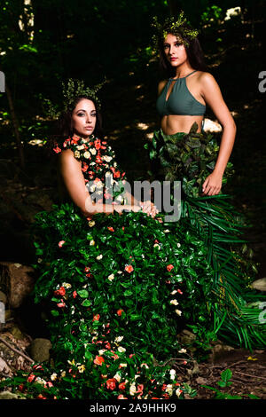Outdoor di alta moda di due donne 1 in un abito di fiori e foglie e gli altri in un mantello di foglie. Entrambe presentano progettati in modo personalizzato i pezzi di testa Foto Stock