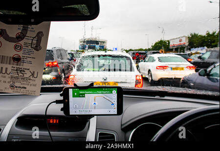 Vista dall'interno di una vettura in attesa per la navetta presso il tunnel sotto la Manica a Folkestone in un giorno di pioggia. Un GPS Sat Nav applicazione su un telefono mobile mostra Foto Stock