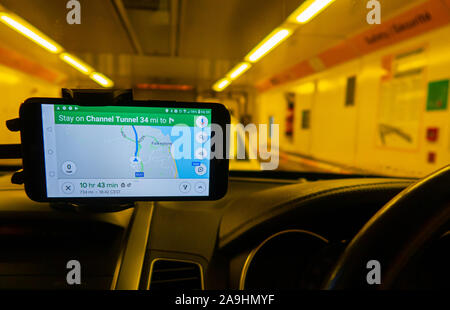 Vista dall'interno di un'auto di una navetta che trasla i veicoli passeggeri attraverso il tunnel del canale. Un navigatore satellitare GPS con montaggio a cruscotto mostra la strada. Foto Stock