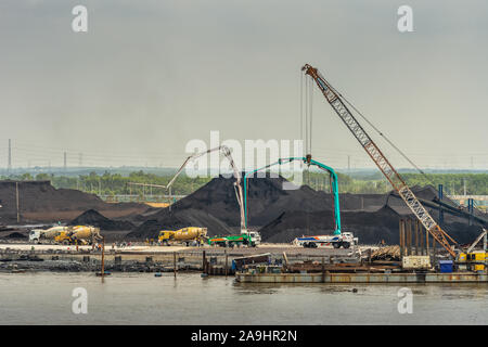 Lungo il fiume Tau, Vietnam - Marzo 12, 2019: Phuoc Khanh area. Primo piano della porta di carbone con banchine e le sue colline del black stuff. Tall gru e t di pompaggio Foto Stock