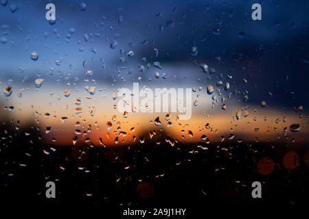 Tramonto colorato attraverso umido vetro di finestra con perline gocce di pioggia e rivoli di acqua su un giorno di tempesta in un frame completo sfondo concettuale Foto Stock