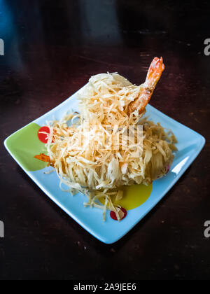 Gamberi fritti rivestiti con tagliatelle note come Udang Sanggul su un piatto colorato su un tavolo di legno. Foto Stock