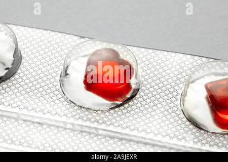 Amore pillole. Confezione blister con il rosso a forma di cuore ad pillole. Compresse per gli amanti o potenza. Sfondo grigio. Foto Stock