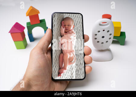 Persona della mano che tiene il telefono cellulare con il bambino immagine presso la videocamera Wireless Foto Stock