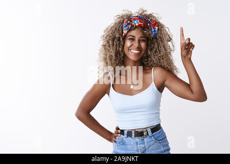 Allegro, entusiasta curly-pelose americano africano donna bionda con naso forato in cima, ridendo e sorridendo cordiale come mostrando un buon luogo appendere pr Foto Stock