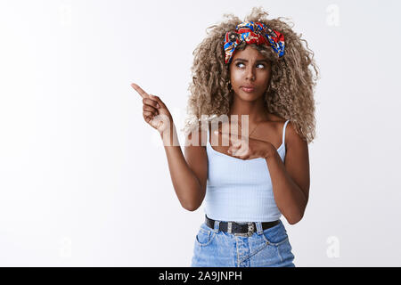 Certi ponderando attraente AFRICAN-AMERICAN curly-pelose ragazza bionda con archetto, cercando esitanti e scomoda, rivolta a sinistra dubbia, fissando Foto Stock