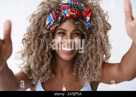 Close-up friendly, sorridenti afro-americano con la ragazza bionda capelli ricci, tendere le mani avanti, tenere la fotocamera o inclinati di abbraccio, coccole, tenendo c Foto Stock