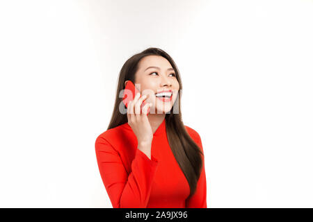 Bella giovane donna asiatica parlando al telefono con qualcuno mentre indossa red Ao Dai. Isolato su sfondo bianco Foto Stock