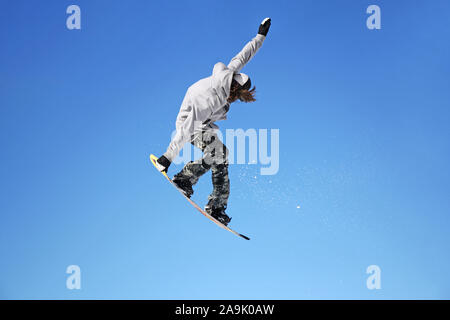 Snowboarder jumping attraverso aria con cielo blu in background Foto Stock