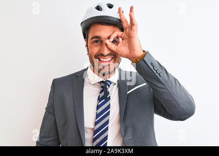 Bel giovane uomo d affari il casco protettivo e auricolari wireless su sfondo isolata facendo ok gesto con la mano sorridendo, occhio guardando attraverso il dito Foto Stock
