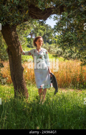 Donna in 40's vestiti sotto un albero di olivo nella campagna abruzzese con un campo di grano in background Foto Stock