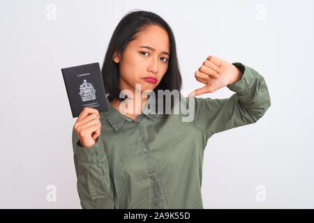 Bella donna cinese holding Canada passaporto canadese isolato su sfondo bianco con volto arrabbiato, segno negativo che mostra antipatia con i pollici dow Foto Stock