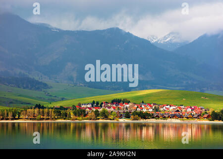 Villaggio sulle rive di un lago. bellissimo paesaggio rurale in montagna. lontane cime coperte di neve in nubi. fantastico scenario della western Alti Tatra i Foto Stock