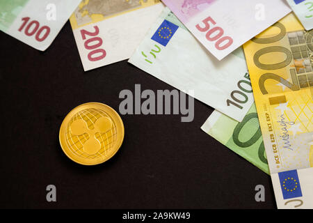 Ripple coin accanto alle banconote in euro su sfondo nero. Valuta digitale, catena di blocco di mercato. Euro Bills accanto alla moneta crypto Foto Stock