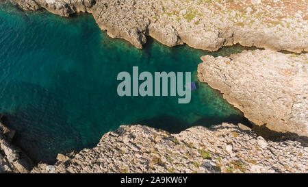 Vista aerea del mare turchese delle acque in una grotta rocciosa, con blu letto gonfiabile floating vicino alla riva. Foto Stock