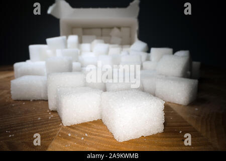 Macro shot di cubetti di zucchero accanto alla scatola di cartone sul tavolo di legno. Cibo malsano dolcificante, dolci cubetti di cristallo Foto Stock